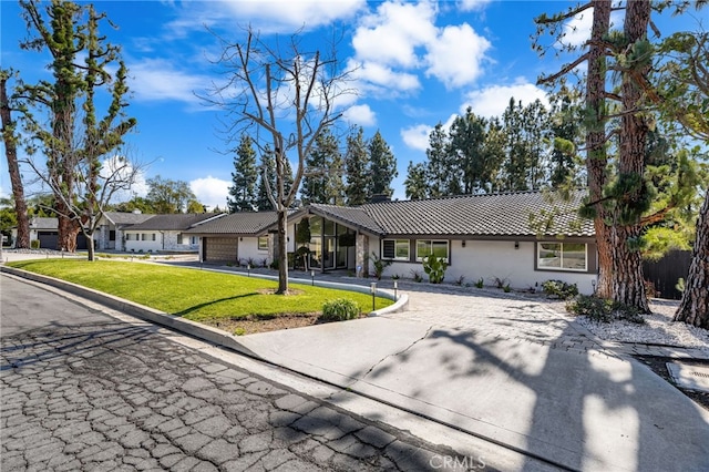 ranch-style home with a tiled roof, stucco siding, driveway, and a front lawn