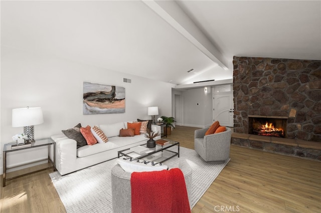 living area with wood finished floors, visible vents, baseboards, vaulted ceiling with beams, and a stone fireplace