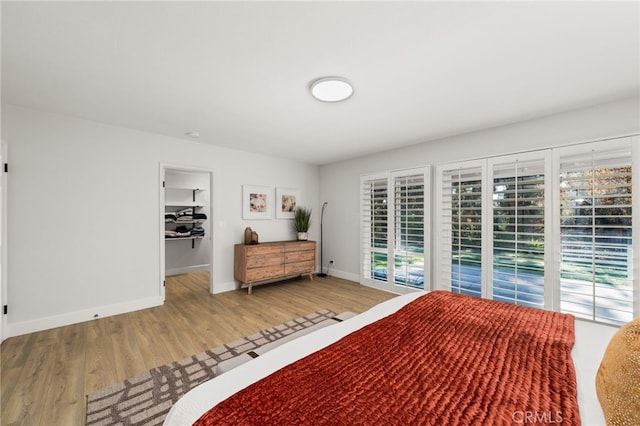 bedroom featuring baseboards, wood finished floors, and a spacious closet