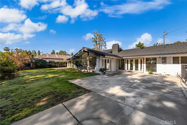 back of property with fence, french doors, a yard, a chimney, and a tiled roof