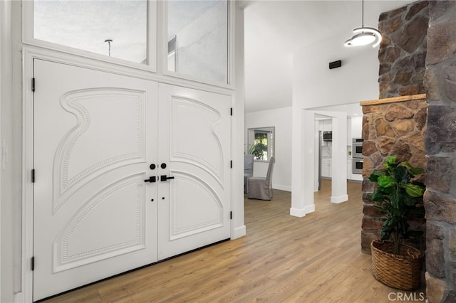 entryway featuring baseboards, light wood-type flooring, and a towering ceiling