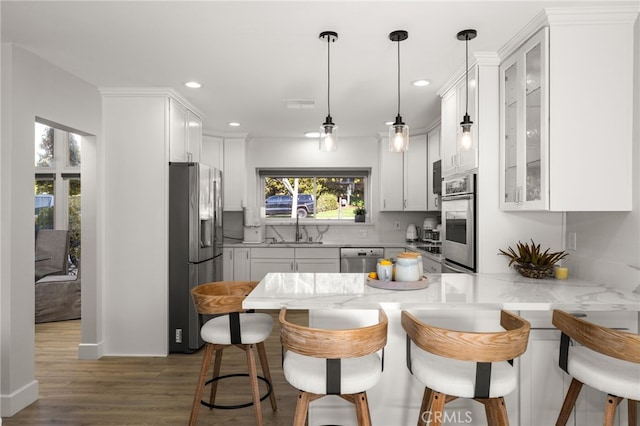 kitchen featuring a sink, wood finished floors, stainless steel appliances, a peninsula, and a breakfast bar area