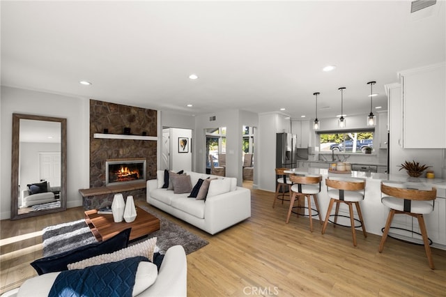 living area with a stone fireplace, recessed lighting, and light wood-style floors