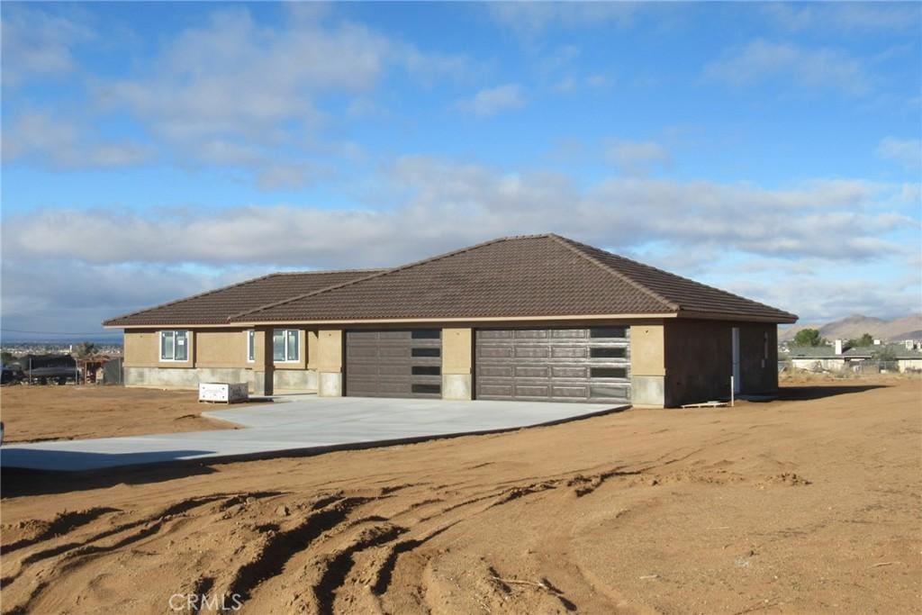 view of front facade featuring a tiled roof, a garage, driveway, and stucco siding