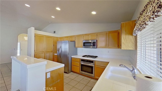 kitchen featuring vaulted ceiling, light tile patterned floors, arched walkways, stainless steel appliances, and a sink