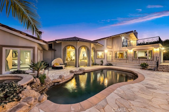 pool at dusk featuring a jacuzzi, a patio area, and an outdoor pool