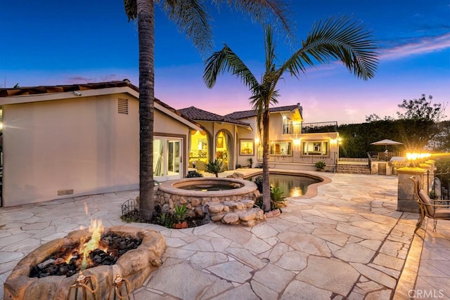 patio terrace at dusk with an in ground hot tub, a balcony, a fire pit, and french doors