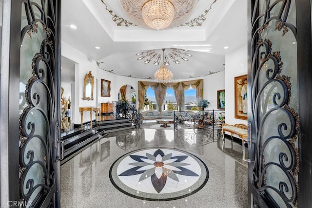 entrance foyer featuring a chandelier, a tray ceiling, recessed lighting, arched walkways, and speckled floor