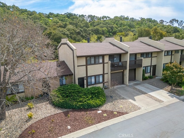 view of front of property featuring stucco siding, roof with shingles, concrete driveway, an attached garage, and a balcony