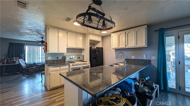 kitchen featuring gas range gas stove, a peninsula, black refrigerator with ice dispenser, white cabinets, and a sink