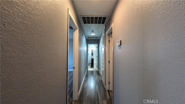 hallway with wood finished floors, a textured wall, and visible vents