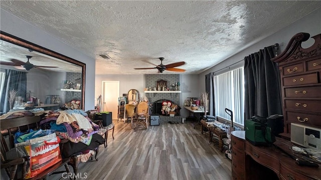 living area with wood finished floors, visible vents, ceiling fan, a textured ceiling, and a brick fireplace