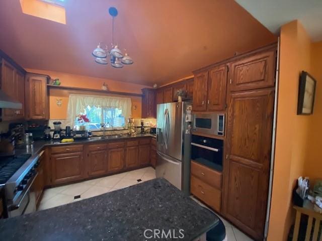 kitchen with brown cabinetry, an inviting chandelier, light tile patterned flooring, a sink, and stainless steel appliances