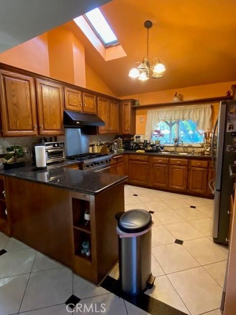 kitchen with under cabinet range hood, stove, brown cabinetry, and freestanding refrigerator