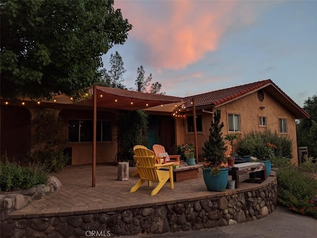 back of house at dusk featuring a tile roof, a patio area, and stucco siding