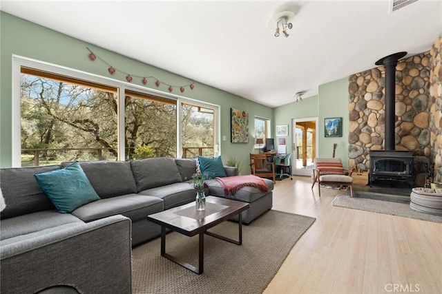 living area featuring vaulted ceiling, a wood stove, visible vents, and wood finished floors