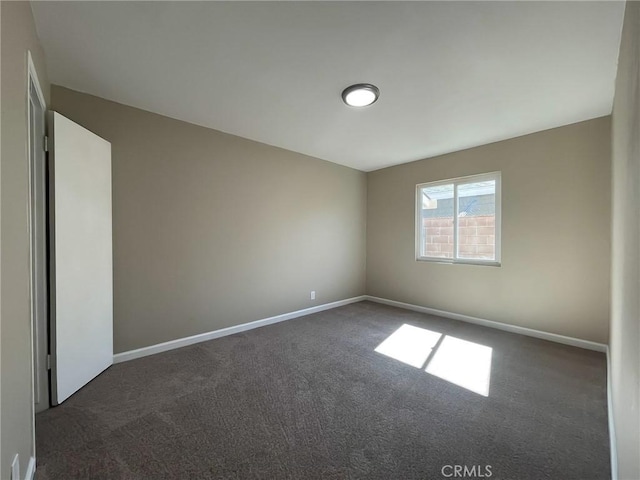 unfurnished room featuring baseboards and dark colored carpet