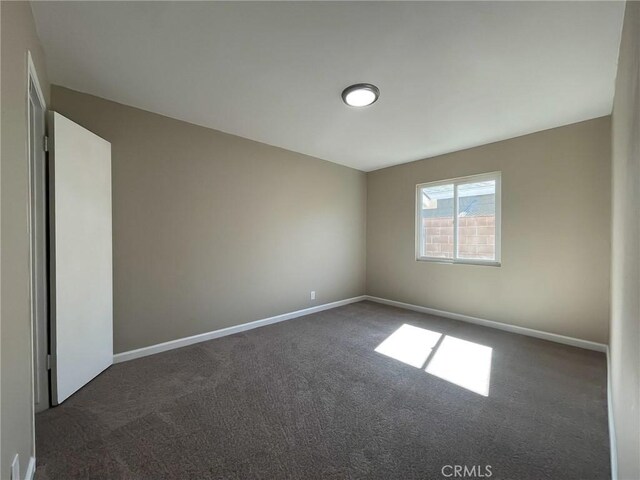 unfurnished room with dark carpet and baseboards