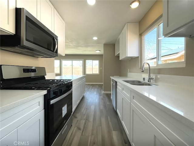 kitchen with light countertops, stainless steel appliances, wood finished floors, white cabinetry, and a sink