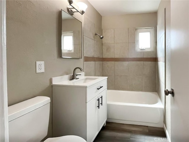 bathroom featuring toilet, wood finished floors, bathtub / shower combination, a textured wall, and vanity