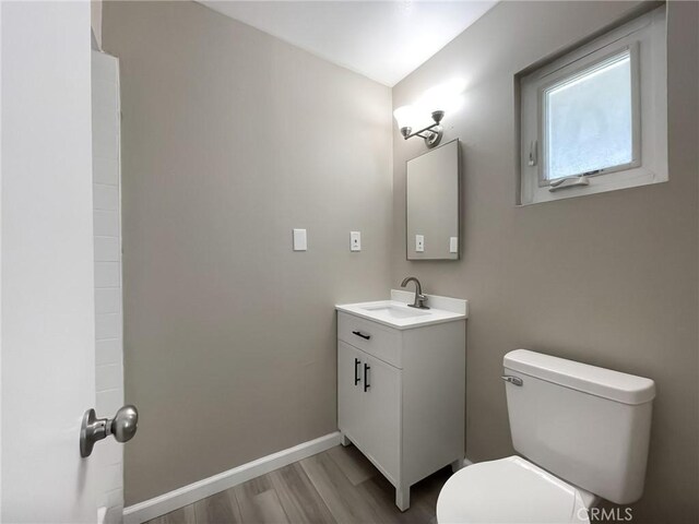 bathroom featuring baseboards, toilet, wood finished floors, and vanity