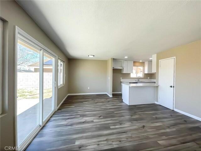 interior space featuring baseboards, light countertops, a peninsula, dark wood-style floors, and white cabinets