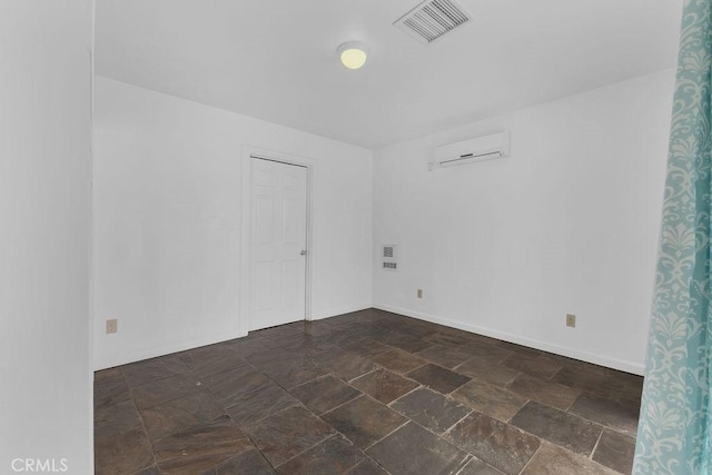 empty room featuring a wall mounted air conditioner, visible vents, baseboards, and stone finish flooring