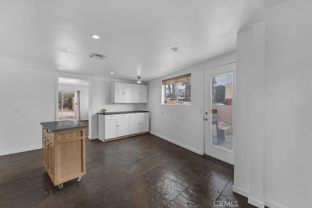 kitchen featuring visible vents, dark countertops, stone tile flooring, white cabinets, and baseboards