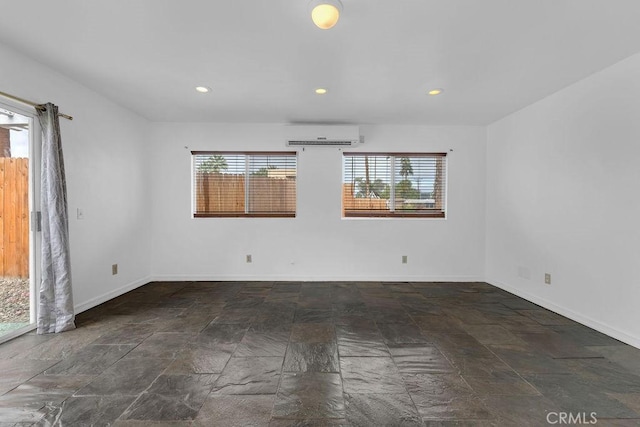 spare room featuring a wall mounted air conditioner, recessed lighting, baseboards, and a wealth of natural light