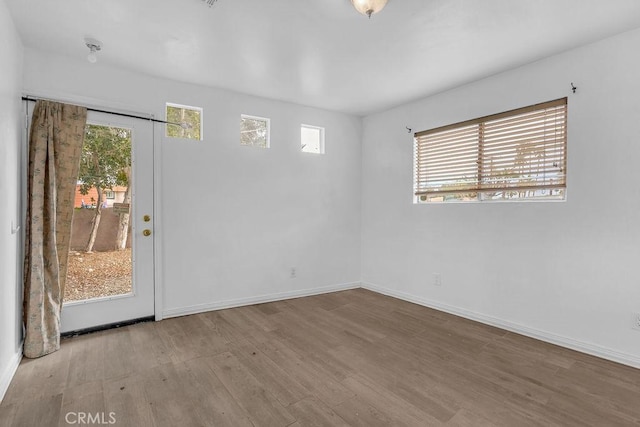 empty room with plenty of natural light, wood finished floors, and baseboards