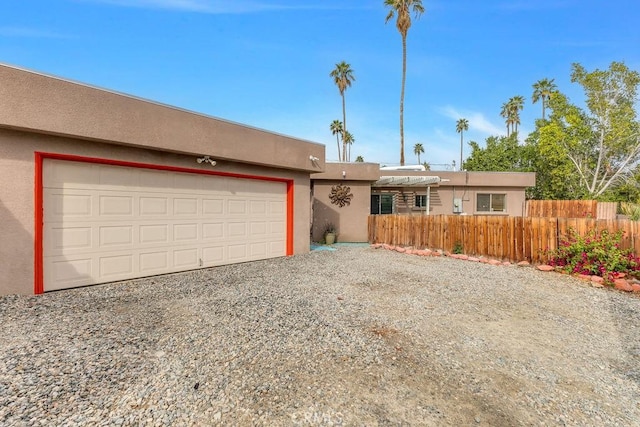 view of front of home featuring gravel driveway, fence, a garage, and stucco siding