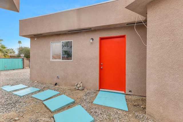 doorway to property with stucco siding and fence