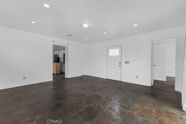 spare room featuring recessed lighting, stone finish floor, baseboards, and a barn door