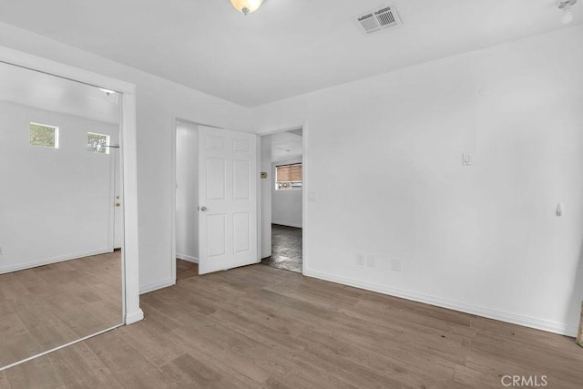 unfurnished bedroom with visible vents, multiple windows, baseboards, and wood finished floors