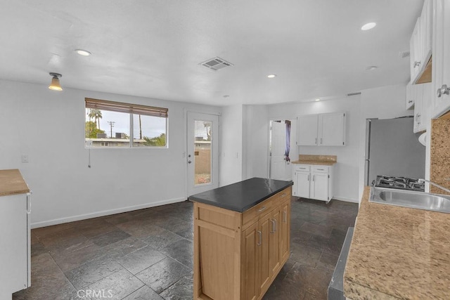 kitchen featuring stone tile flooring, visible vents, freestanding refrigerator, and a sink