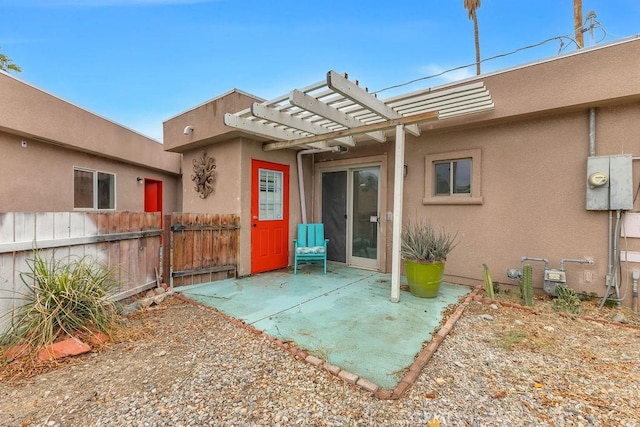 doorway to property featuring stucco siding, a patio, a pergola, and fence