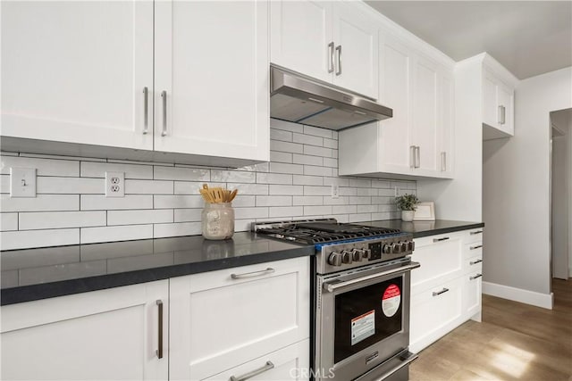 kitchen featuring stainless steel range, under cabinet range hood, dark countertops, white cabinetry, and decorative backsplash