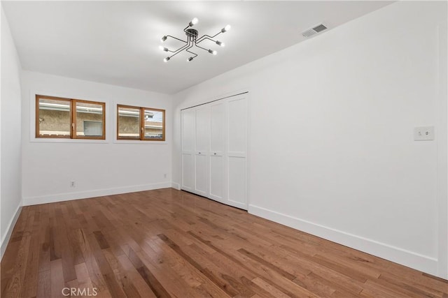 unfurnished bedroom featuring visible vents, a notable chandelier, hardwood / wood-style flooring, a closet, and baseboards