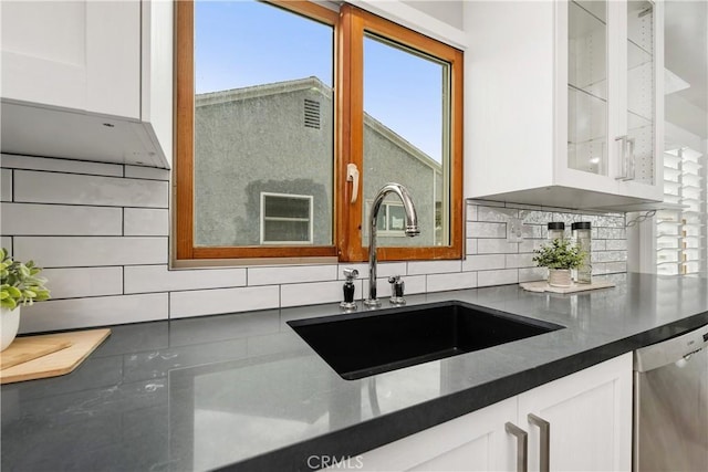 kitchen featuring a sink, white cabinets, glass insert cabinets, dishwasher, and dark countertops