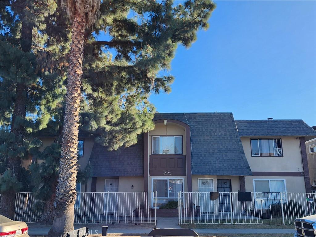 view of property with stucco siding, roof with shingles, and fence