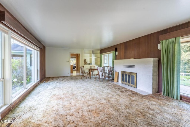 unfurnished living room with carpet floors, a brick fireplace, and wood walls