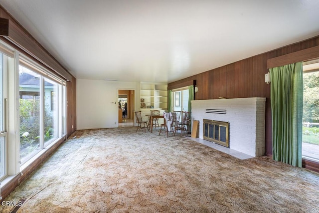 unfurnished living room featuring carpet, a brick fireplace, and wooden walls