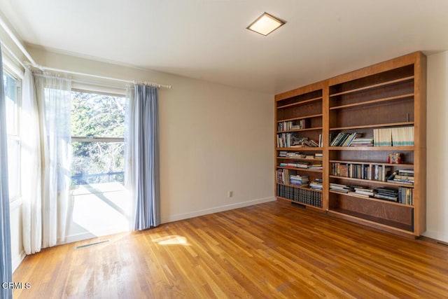 spare room with built in shelves, wood finished floors, and baseboards