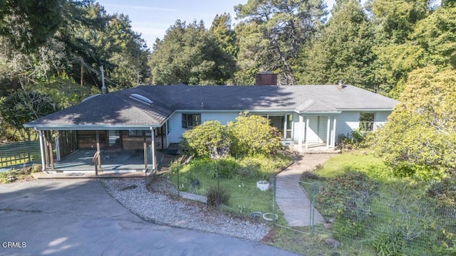 ranch-style house featuring a carport, fence, driveway, and a chimney