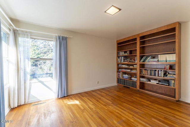 empty room featuring visible vents, wood finished floors, and baseboards
