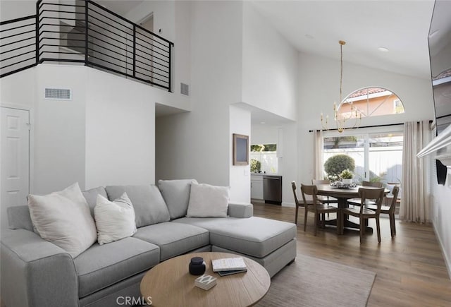 living room featuring a notable chandelier, wood finished floors, visible vents, and high vaulted ceiling