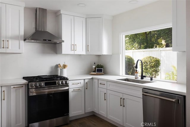 kitchen with a sink, appliances with stainless steel finishes, wall chimney exhaust hood, and white cabinets