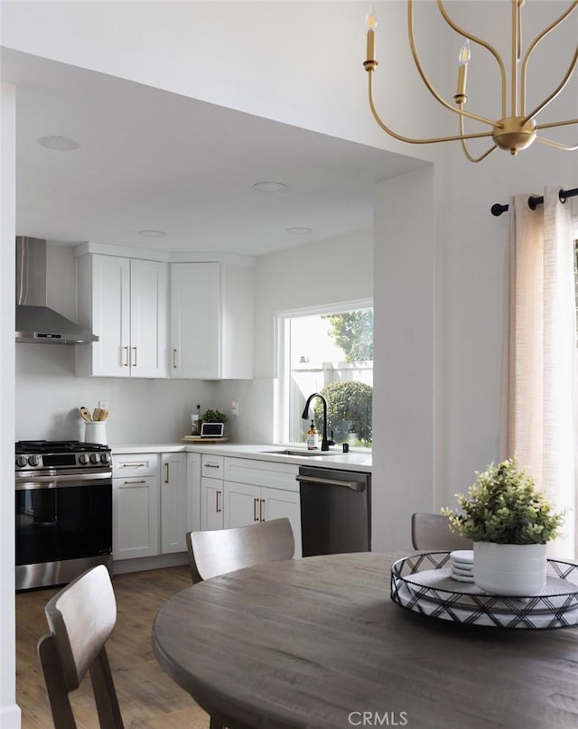 kitchen with dishwashing machine, an inviting chandelier, white cabinets, gas range, and wall chimney range hood