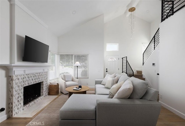 living area featuring wood finished floors, baseboards, high vaulted ceiling, stairs, and a tiled fireplace