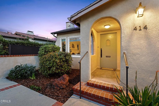 exterior entry at dusk featuring fence and stucco siding